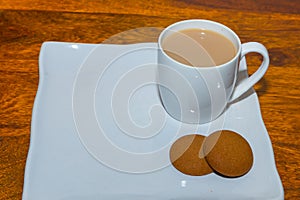 A white cup with tea or coffee along with cookies kept on a wooden table