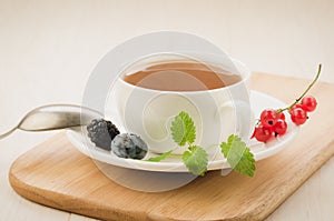 white cup tea and with leaves of mint and berries in a saucer/white cup tea and with leaves of mint and berries in a saucer on a