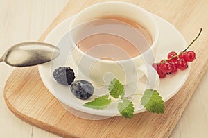 White cup tea and with leaves of mint and berries in a saucer/white cup tea and with leaves of mint and berries in a saucer on a