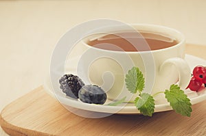 White cup of tea with leaves of mint and berries in a saucer on a wooden tray/white cup of tea with leaves of mint and berries in