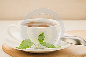 white cup of tea and leaves of mint in a saucer and spoon/white cup of tea and leaves of mint in a saucer and spoon on a wooden