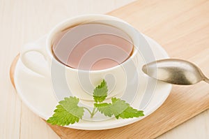 White cup of tea and leaves of mint in a saucer and spoon on a wooden background/white cup of tea and leaves of mint in a saucer