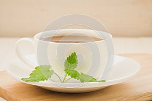 white cup of tea and leaves of mint in a saucer on a wooden background/white cup of tea and leaves of mint in a saucer on a wooden