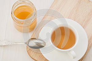 white cup of tea with an open jar of honey/white cup of tea with an open jar of honey on a wooden tray. Top view