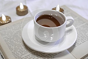 White cup of tea with a saucer, closeup. Open old book. Yellow sheets of pages. The study of science. Reading. White background. B