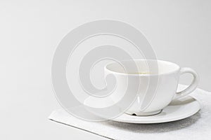 white cup with tea on a saucer on a napkin on a light background.