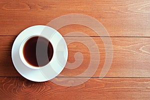 White cup with tea on a saucer. On wooden brown background