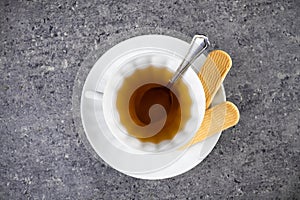 White cup of tea with spoon and saucer with two cookies. On granite surface