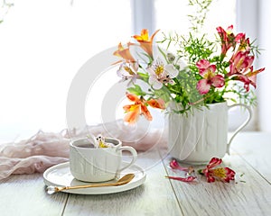 White cup with tea on the table. Flowers nearby