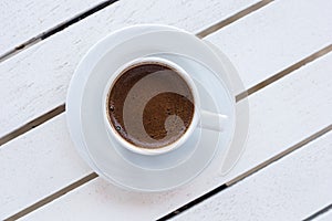 White cup of Turkish coffee on saucer on light wooden table. Top view with copy space. Lifestyle background