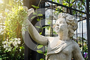 White cupid statue holding a bird on the hand in the green garden.Thailand.