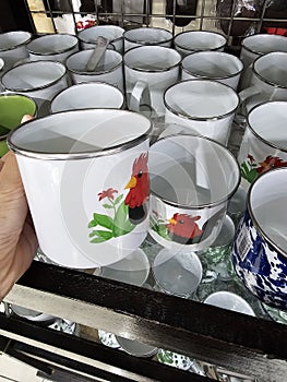 White cups displayed for sale, adorned with cartoon images of a black rooster with red wattles and green foliage photo