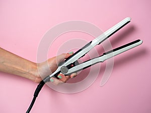 White curling iron in a woman`s hand on a pnk background. An accessory for creating hairstyles. Beauty and fashion. Hair care