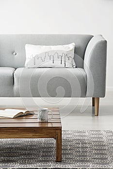 White cushion on grey sofa in minimal living room interior with wooden table on carpet. Real photo