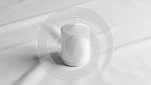 White cylindrical candle placed on a smooth white fabric surface