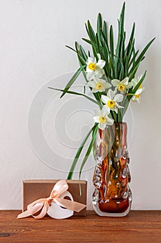 White daffodils flowers and gift box with pink ribbon greeting card on light background. Place text 8 March Mothers Day