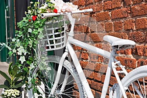 White decorative old bike with a basket of flowers against a brick wall. Copy space