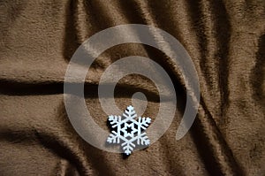 White decorative snowflake on brown plush background with copy space. Winter abstract background. Fluffy fabric surface.