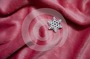 White decorative snowflake on pink plush background with copy space. Winter abstract background. Fluffy fabric surface. Top view,