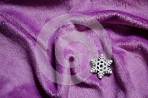 White decorative snowflake on purple plush background with copy space. Winter abstract background. Fluffy fabric surface.