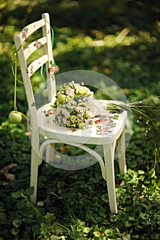 White decoupage chair with green bridal bouquet. Green grass at the apple garden, wedding ceremony. Summer wedding. Soft blur boke