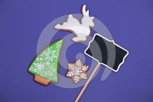 White deer shaped, christmas tree and snowflake shaped gingerbread cookie and space for text on purple background, top view.