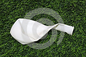 A white deflated balloon on a green artificial grass