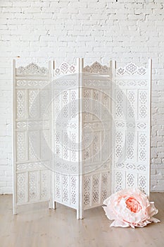 White delicate decorative wood panel with big paper flowers on white brick wall.