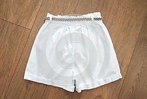 White denim shorts with a striped braided belt on a wooden background. Rear view