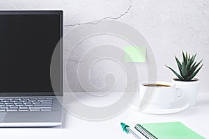 White desk with laptop,  cup of coffee and green notebook and pen