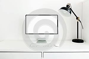 White desktop with blank white monitor and desk lamp. Workplace concept. Mock up blank computer screen with keyboard.