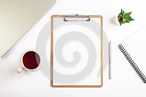 White desktop with clipboard, cup of tea, pencil, notebook and succulent plant. Flat lay, top view, mockup