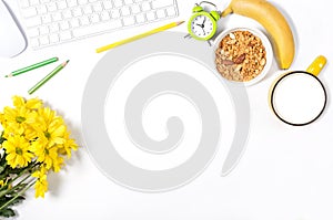 White desktop with keyboard, mouse, colorful stationery, yellow flowers, plate with granola, banana and large cup of milk