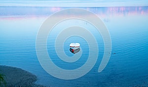 White dinghy afloat on calm blue water with reflection of sunset colors