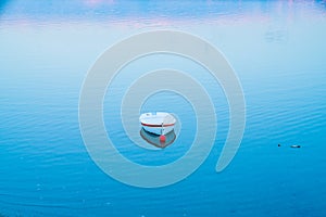 White dinghy afloat on calm blue water with reflection of sunset colors