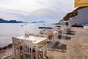 White dining tables on the sea shore with impressing sea view and Klima fishermen village in the background on Milos Island,Greece photo