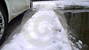 White Dirty Car parking on snow road with puddle. Messy, salt, chemicals in early spring. Tire. Ecology problem in city.