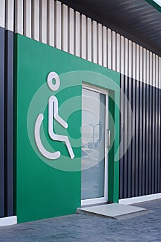 White disabled wheelchair sign with glass door on green wall and wooden panel wall decorations in public restroom