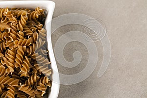 A white dish filled with uncooked wholewheat fusilli pasta