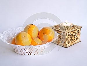 A white dish of oranges next to a box with a small decorative candle on it