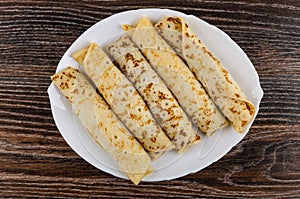 White dish with pancake rolls on wooden table. Top view