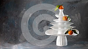 White dishes Pyramid like Christmas tree with mandarins with leaves on top, bunch below on dark Creative concept