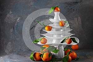 White dishes Pyramid like Christmas tree with mandarins with leaves on top, bunch below on dark Creative concept