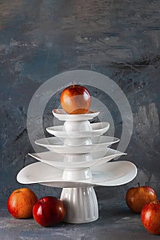 White dishes Pyramid like Christmas tree with red apples on top amd next to, on dark background. Creative concept, dishware, veg,