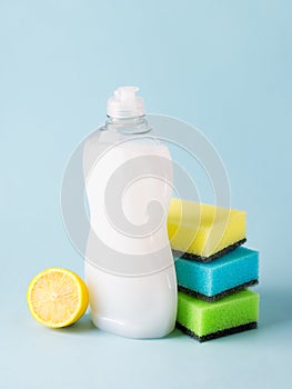 White dishwashing liquid in a plastic bottle, lemon and three foam sponges. Purity and household chemicals. Kitchen detergent on a