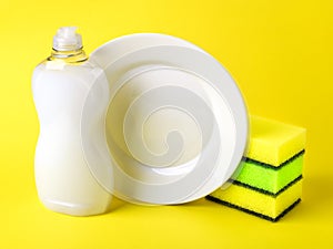 White dishwashing liquid in a plastic bottle, plate and three foam sponges. Purity and household chemicals. Kitchen detergent on a