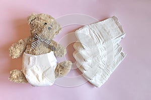 White disposable diapers for little babies on pink background and cute teddy bear. Top view, selective focus