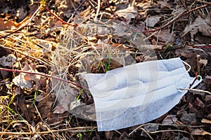 White disposable medical face mask on old dry leaves, thrown away like garbage