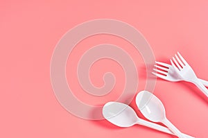 White disposable spoons and forks on pink background