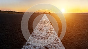 White dividing strip on an asphalt road. Highway. The road goes to the horizon. Sunset